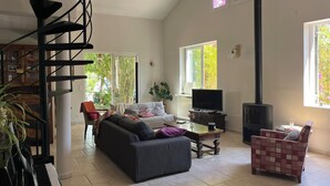 Un salon spacieux comprenant un escalier, un canapé, un téléviseur, une cheminée et un piano.