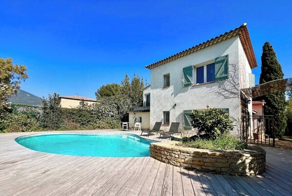 A two-story house with a swimming pool, wooden deck, and stone retaining wall. - Charming villa with swimming pool in a quiet area close to the sea (Toulon)