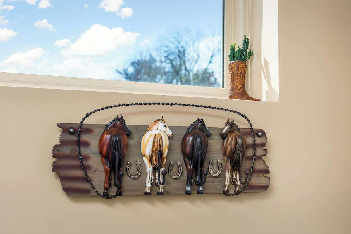 A wall-mounted horse sculpture with a rustic design, positioned above a window with a view of trees and a clear sky.