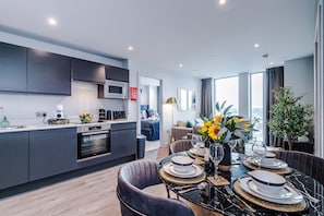 Une cuisine moderne avec des meubles de couleur sombre, un four à micro-ondes et un coin repas avec une table dressée pour quatre personnes.