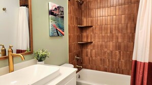 Une salle de bain avec une baignoire, une douche, un lavabo avec un miroir et une étagère fixée au mur.