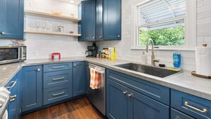 A kitchen with blue cabinets, a stainless steel sink, and a window with a view of greenery. - Fun Midcentury Home | Hot Tub | Karaoke | Games (Lancaster)