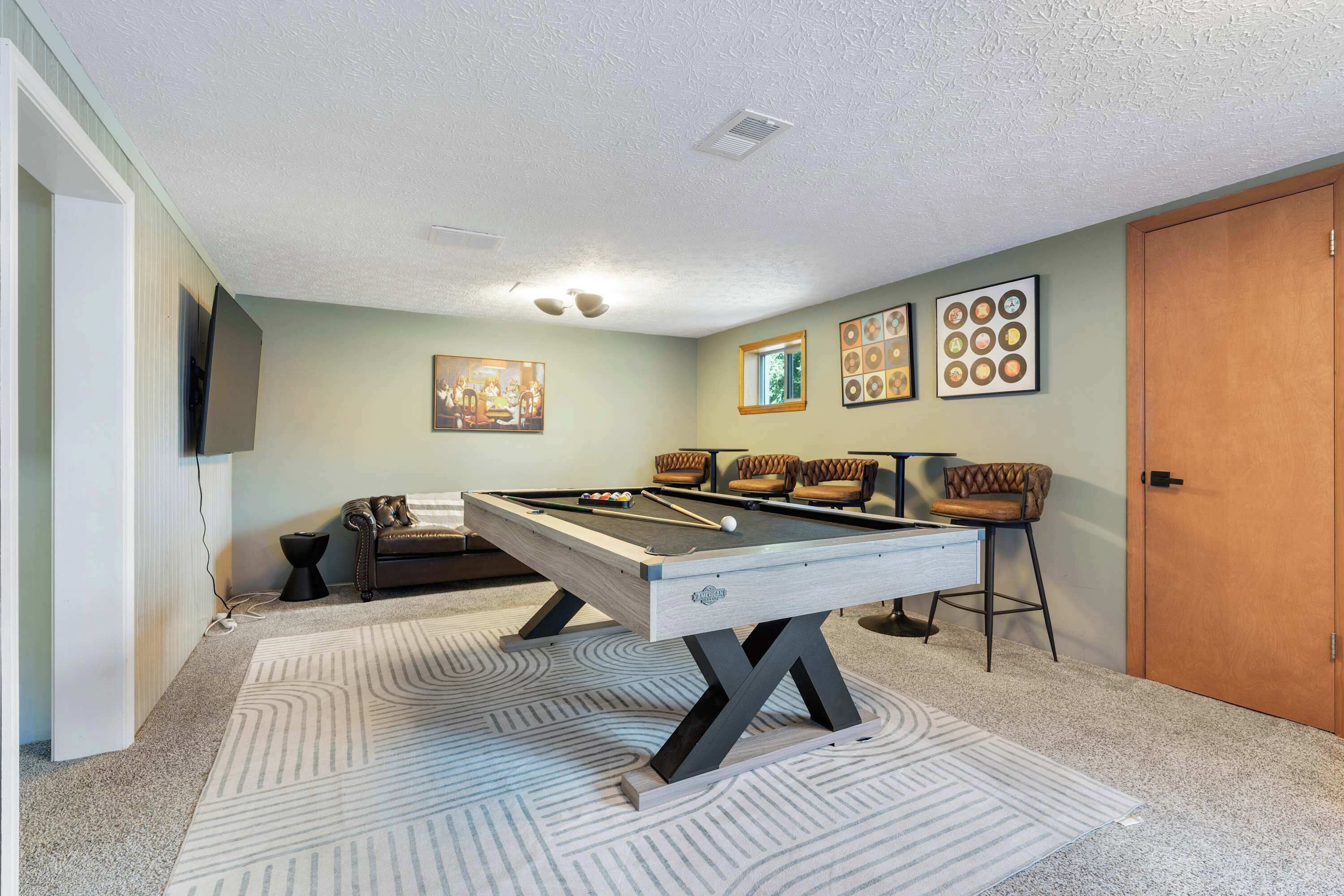 A pool table with a light wood finish and a pool cue, surrounded by four cushioned chairs with a brown leather finish.