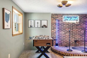 A room with a foosball table, framed pictures on the wall, and a neon sign. - Fun Midcentury Home | Hot Tub | Karaoke | Games (Lancaster)