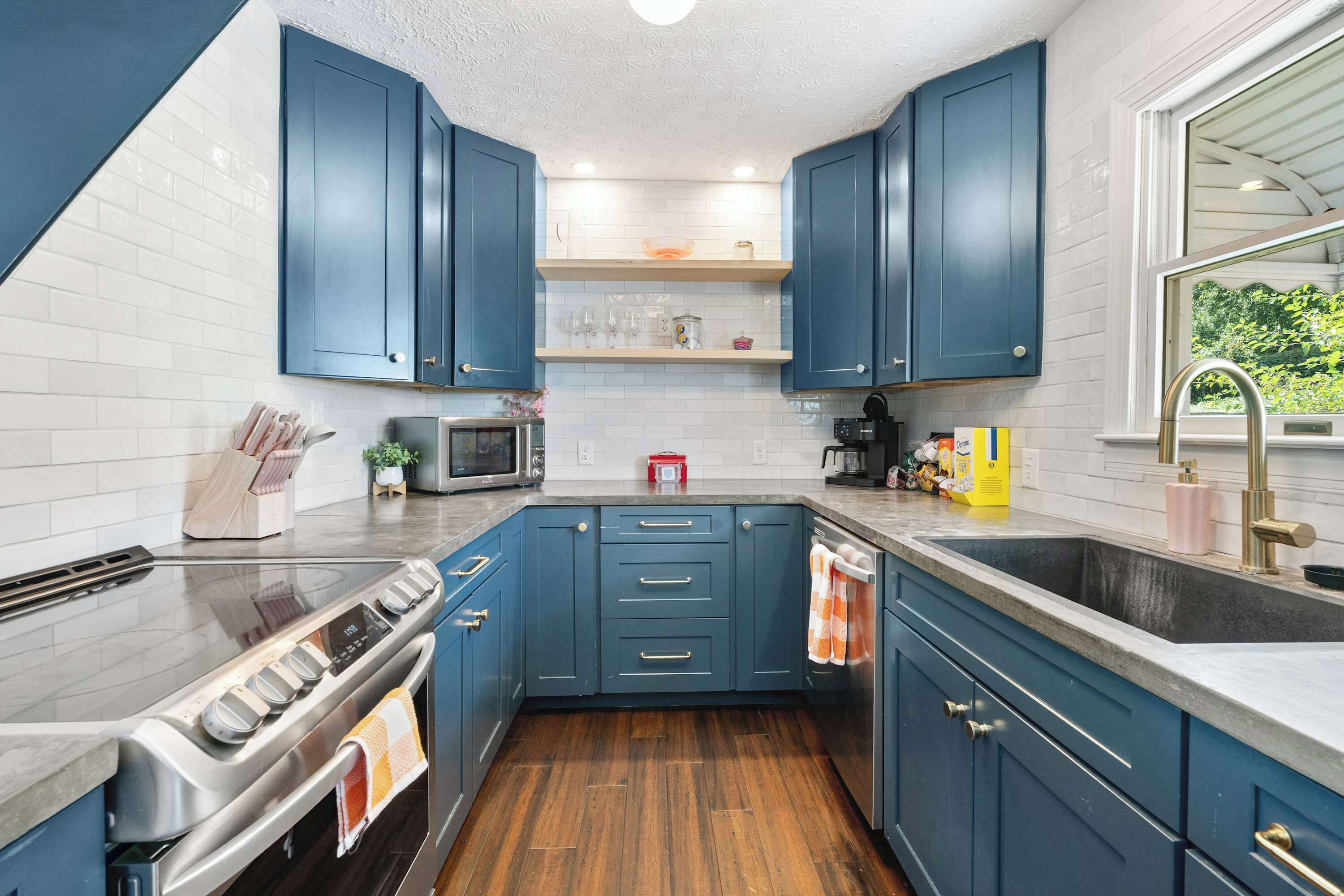 A modern kitchen with blue cabinets, a stainless steel stove, and a window with a view of greenery.