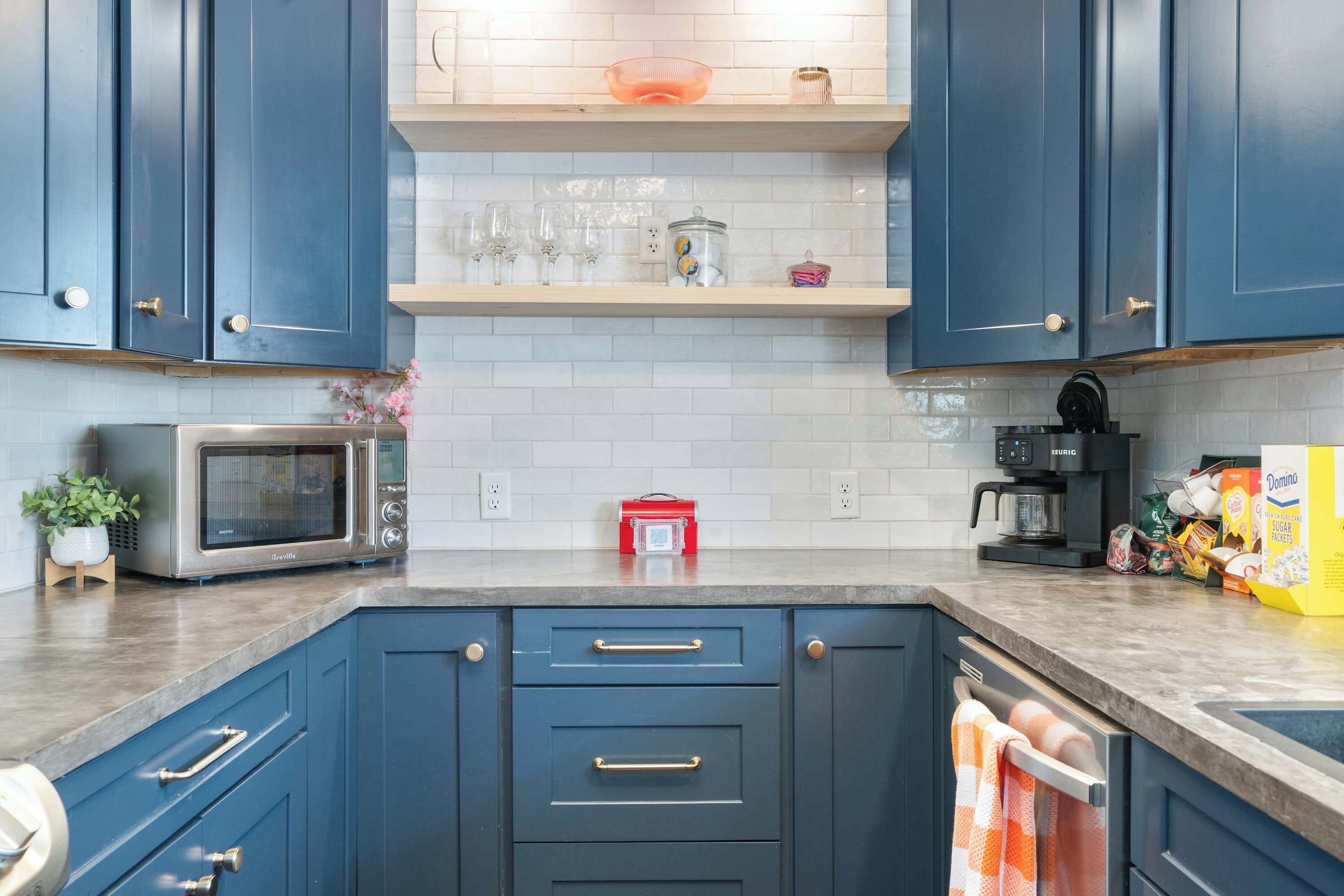 A kitchen with blue cabinets, a microwave, a coffee maker, and a red kettle on the counter.