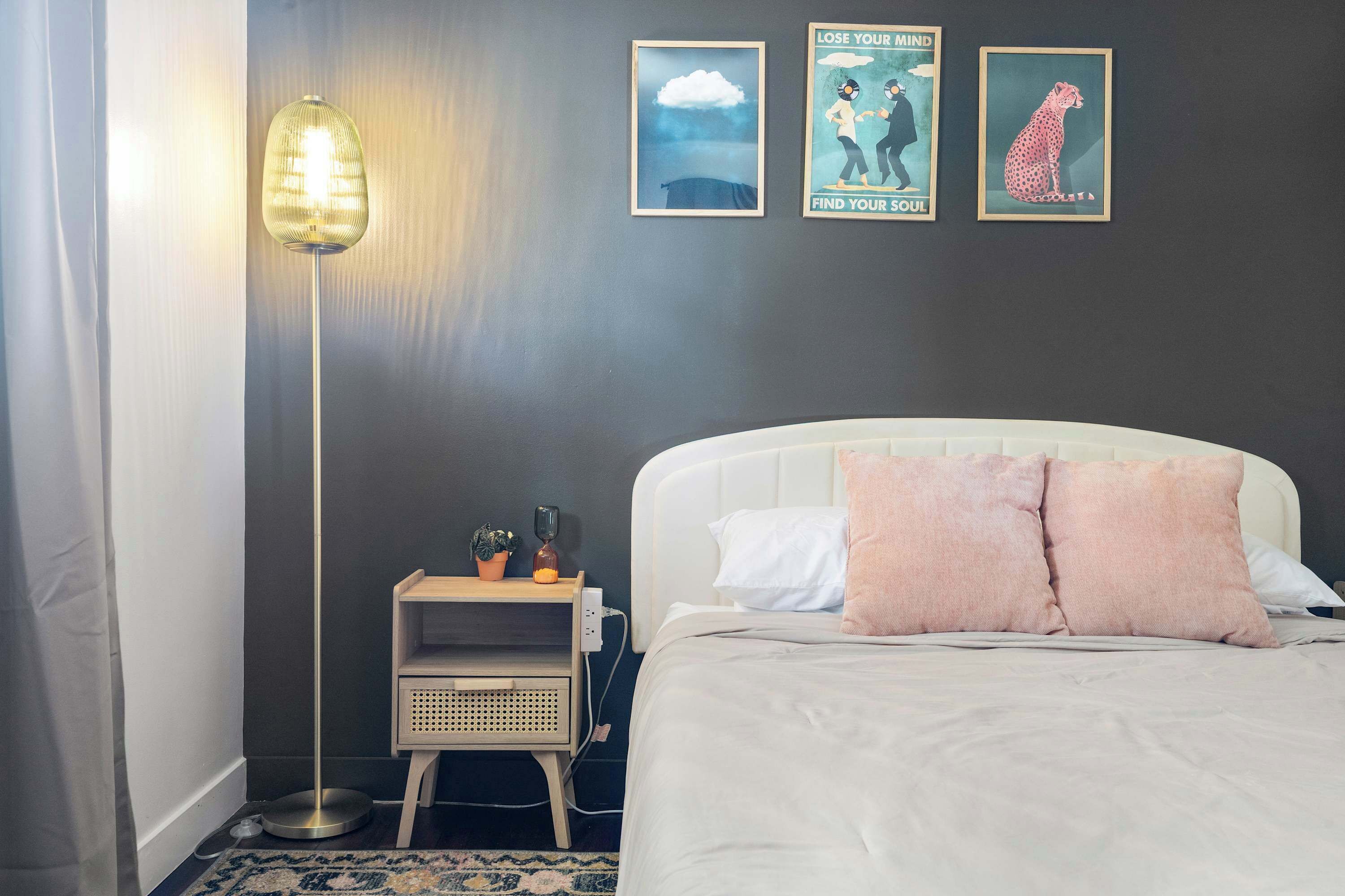 A bedroom with a bed, bedside table, lamp, and wall art.