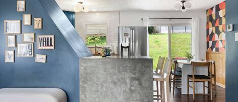 A modern kitchen with a built-in island, a dining area with wooden chairs, and a view of the outdoors.