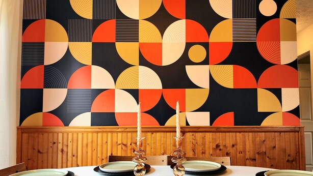 Une table à manger dressée avec des assiettes et des chandeliers, le tout devant un mur orné d’un motif géométrique.