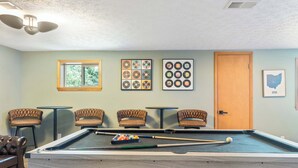 A pool table with billiard balls and cues, surrounded by four cushioned chairs. - Fun Midcentury Home | Hot Tub | Karaoke | Games (Lancaster)