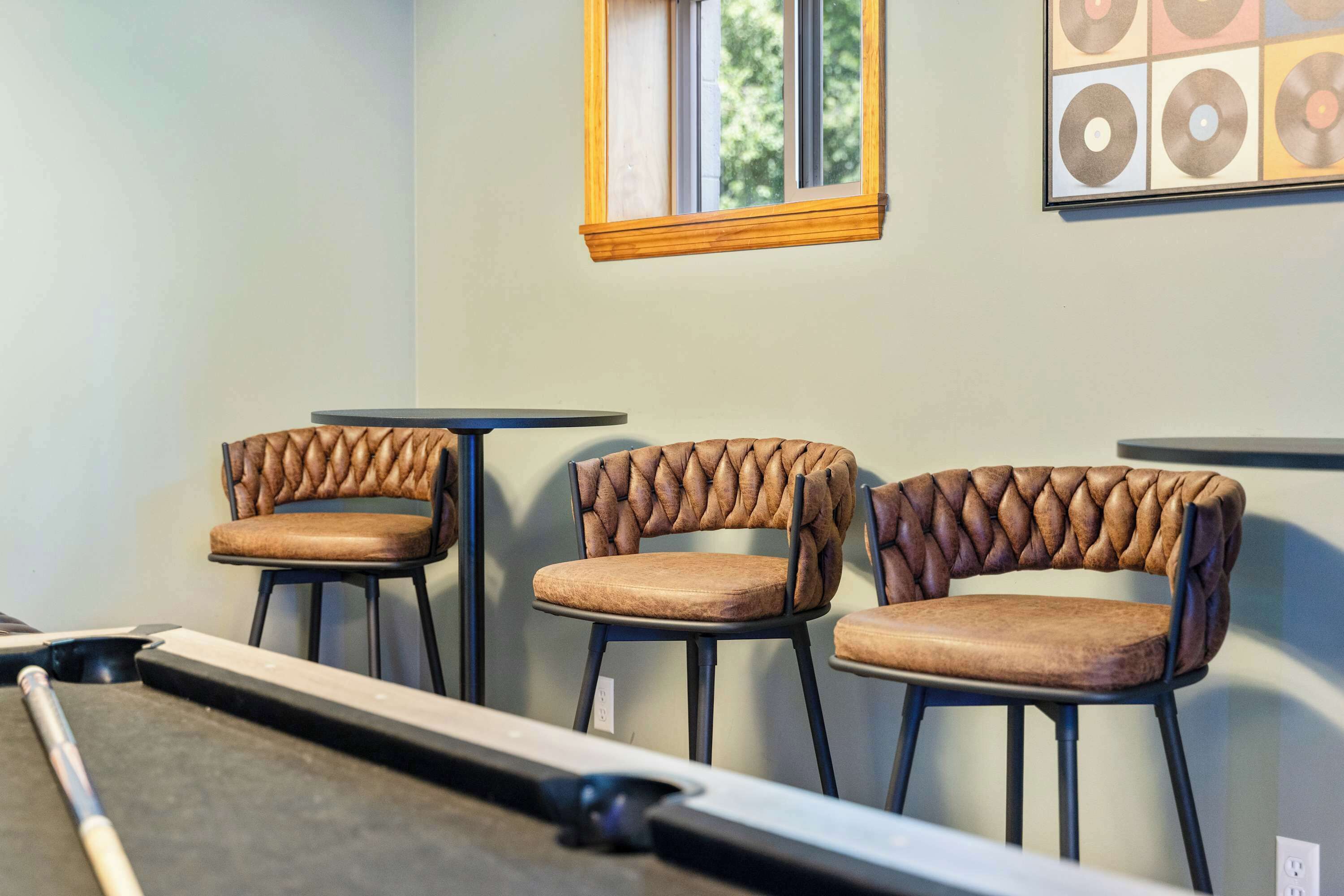 A pool table in a room with three upholstered chairs with a unique braided design.