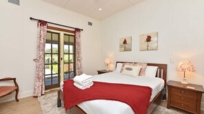 A bedroom with a bed, two bedside tables with lamps, a chair, a window with curtains, and two wall-mounted paintings.