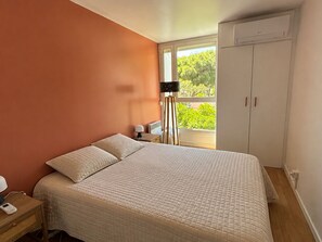 Quarto com cama, mesa de cabeceira, luminária, janela e ar condicionado.
