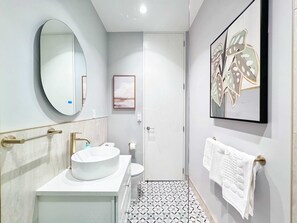 Un baño moderno con un espejo redondo, un lavabo blanco, un inodoro y un suelo estampado.