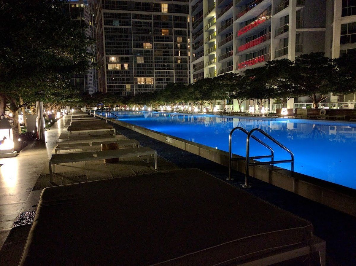 A nighttime swimming pool area with steps leading into the water, surrounded by trees and buildings.
