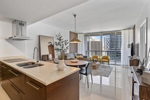 Cozinha moderna com ilha central, área de jantar com mesa redonda e sala de estar com sofá e televisão.