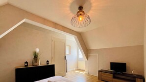 A bedroom with a large bed, a TV, a dresser, and a ceiling light fixture. - La Maison d Utah , Beach and Memory (Sainte-Marie-du-Mont)