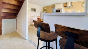 A modern kitchen with a microwave and a clock on the wall. There are two wooden chairs and a small table in the foreground. - La Maison d Utah , Beach and Memory (Sainte-Marie-du-Mont)