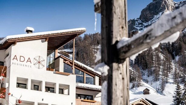 A modern building with a sign reading "ADA RESIDENCE" and a mountain backdrop. - Residence Ada (San Cassiano)