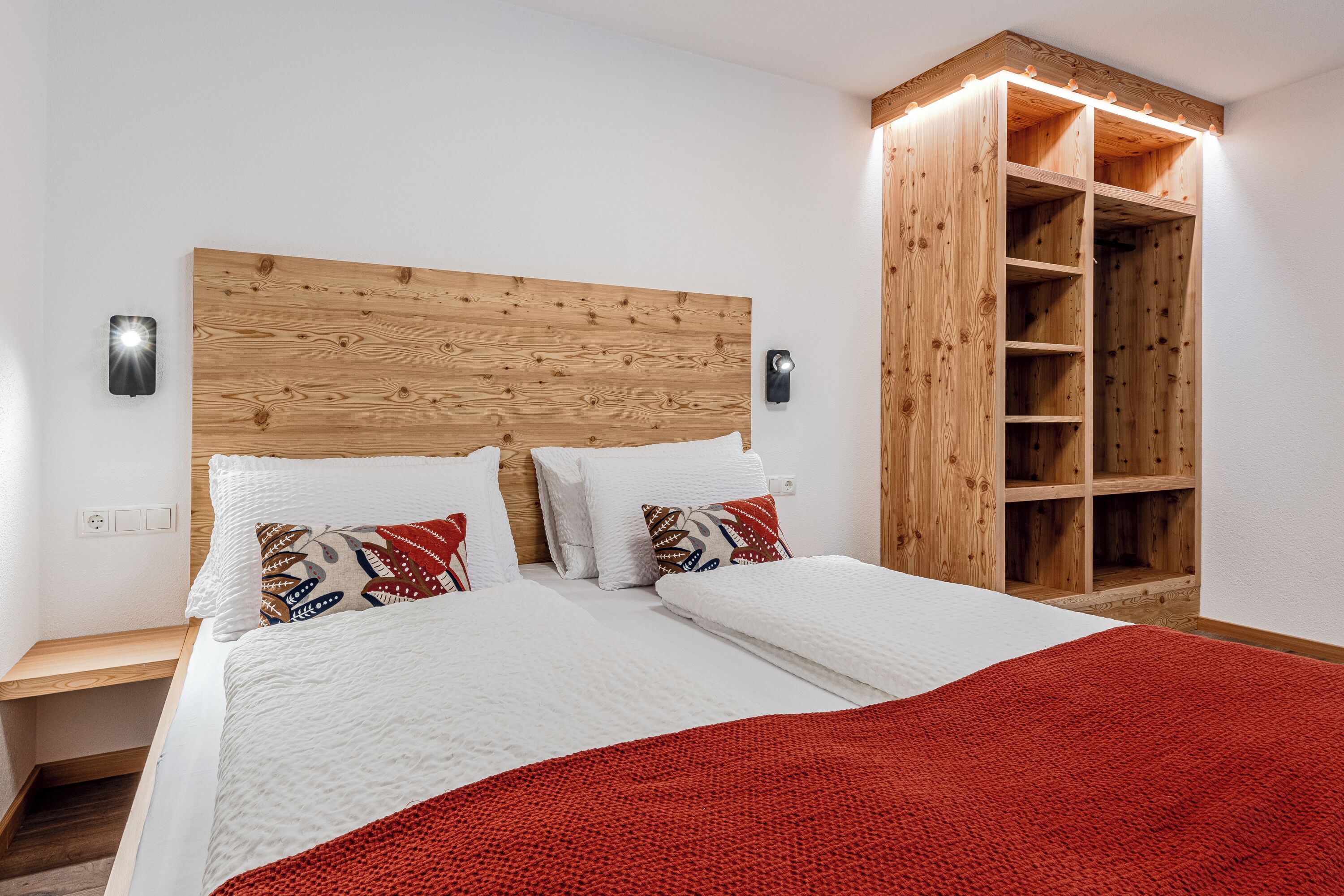 A bedroom with a wooden headboard, a red blanket, and a built-in wooden wardrobe.