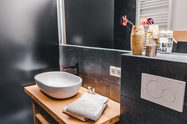 Une salle de bain moderne avec un grand lavabo blanc, un plan de toilette en bois, un miroir et un interrupteur mural.
