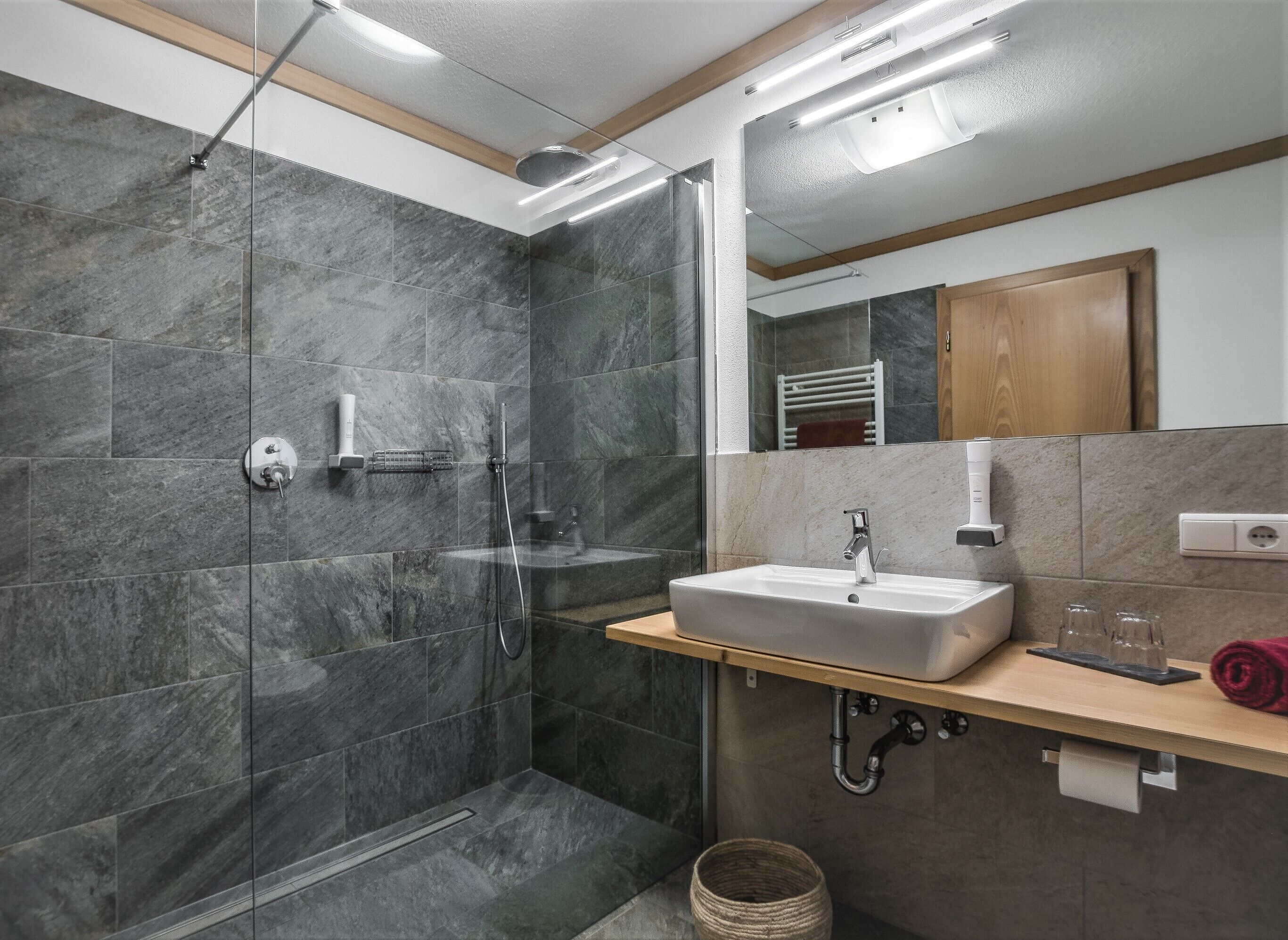 Een moderne badkamer met een douche met glazen wand, een wastafel met spiegel erboven en een handdoekrek.