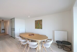 A modern dining area with a round table, six chairs, a whiteboard, and a radiator.