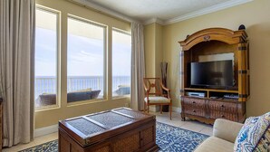 A room with large windows, a television, a wicker chair, and a wooden cabinet. - Gulf Crest 2105b (Panama City Beach)