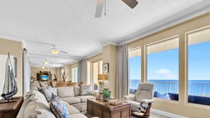 A spacious living room with a large window overlooking the sea, a ceiling fan, and a cozy seating area with a coffee table. - Gulf Crest 2105b (Panama City Beach)