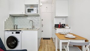 A compact kitchen with a washing machine, microwave, sink, and a dining area with a table and chairs. - Well-equipped studio near the Parc des Princes (Paris)
