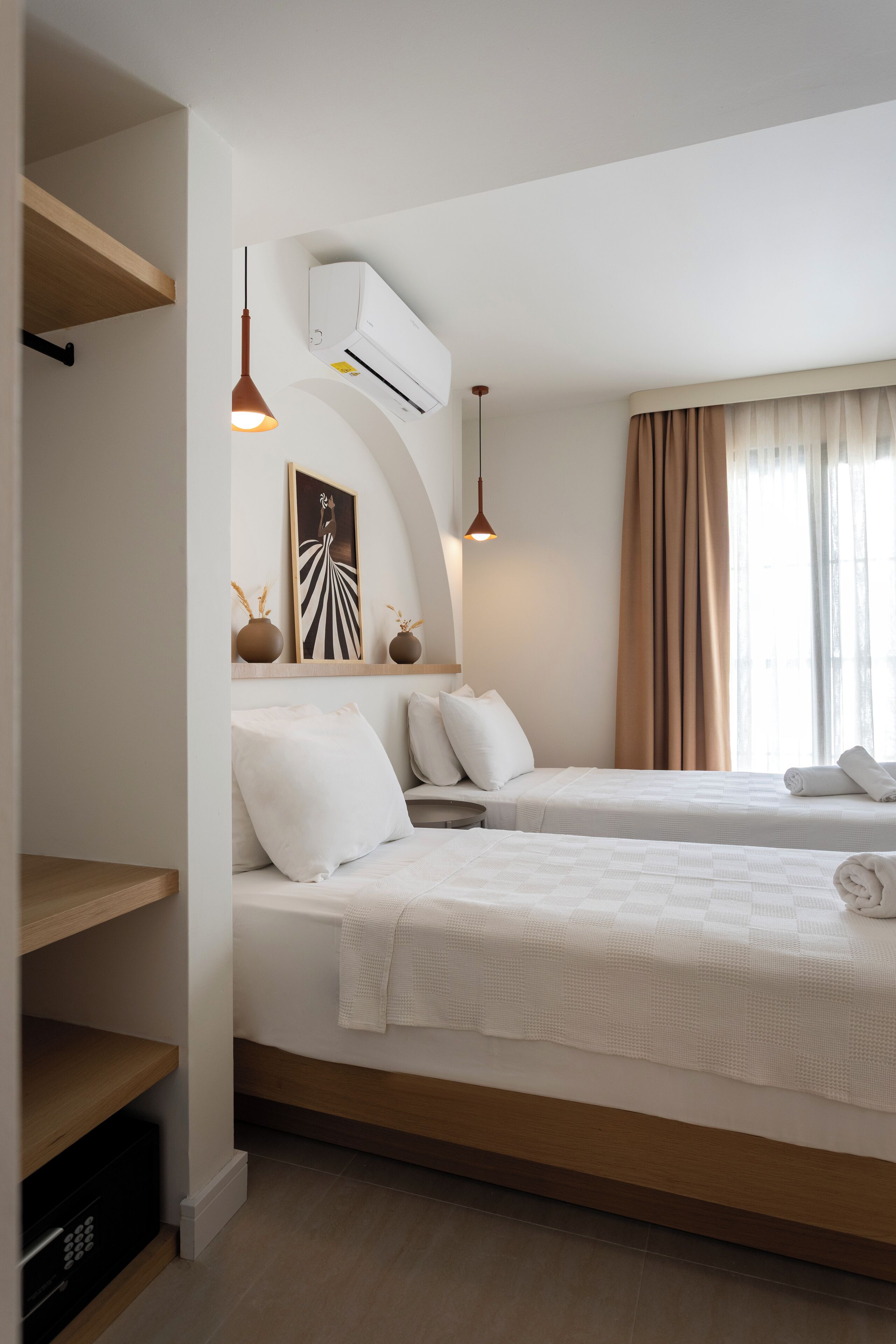A hotel room with two beds, a built-in shelf, a wall-mounted air conditioner, and a pendant light.