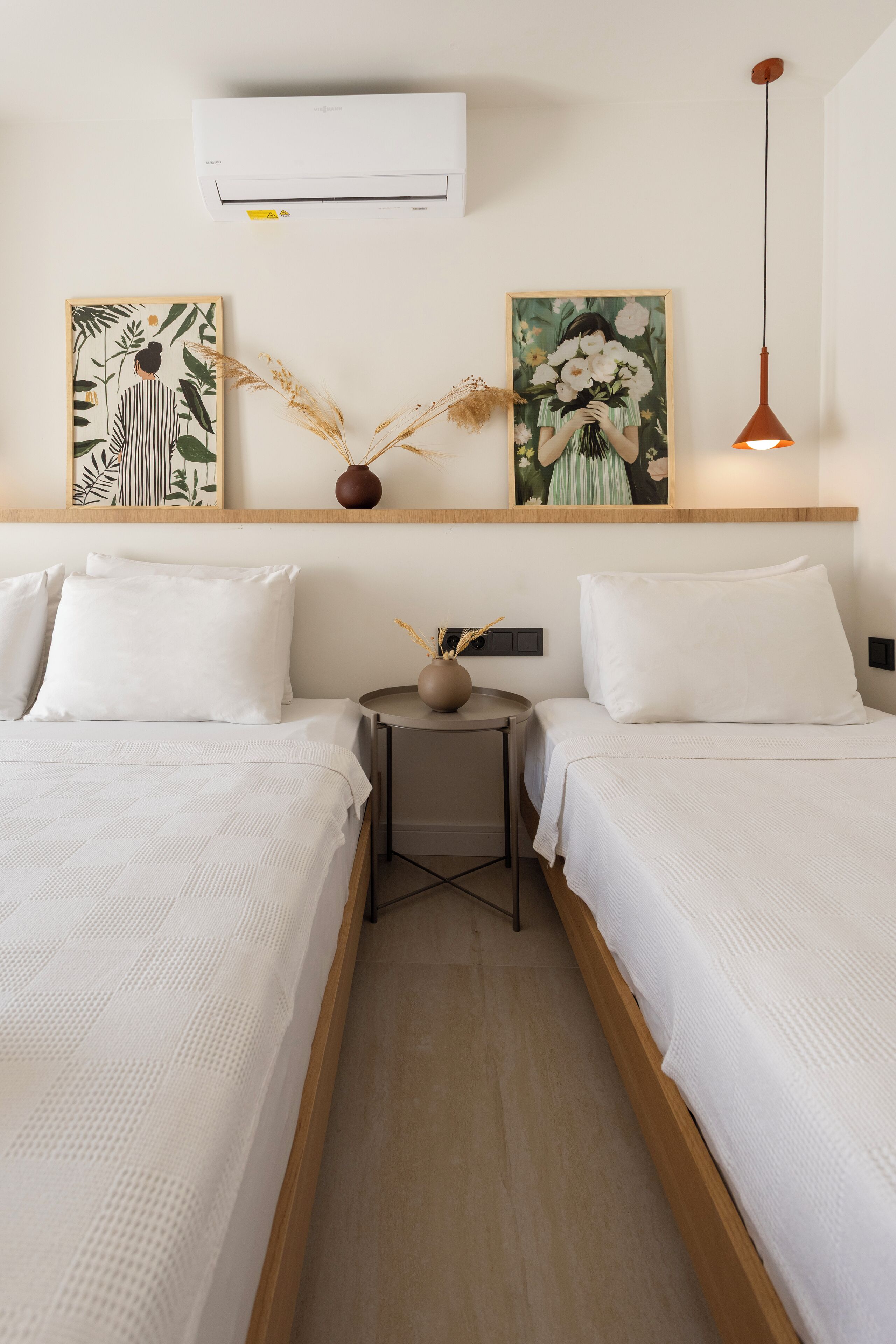 Una habitación de hotel con dos camas, una mesita con un florero y una obra de arte en la pared.