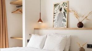 Ein Hotelzimmer mit zwei Betten, einer Pendelleuchte, einem an der Wand befestigten Regal mit Pflanze und einem Nachttisch mit Vase.