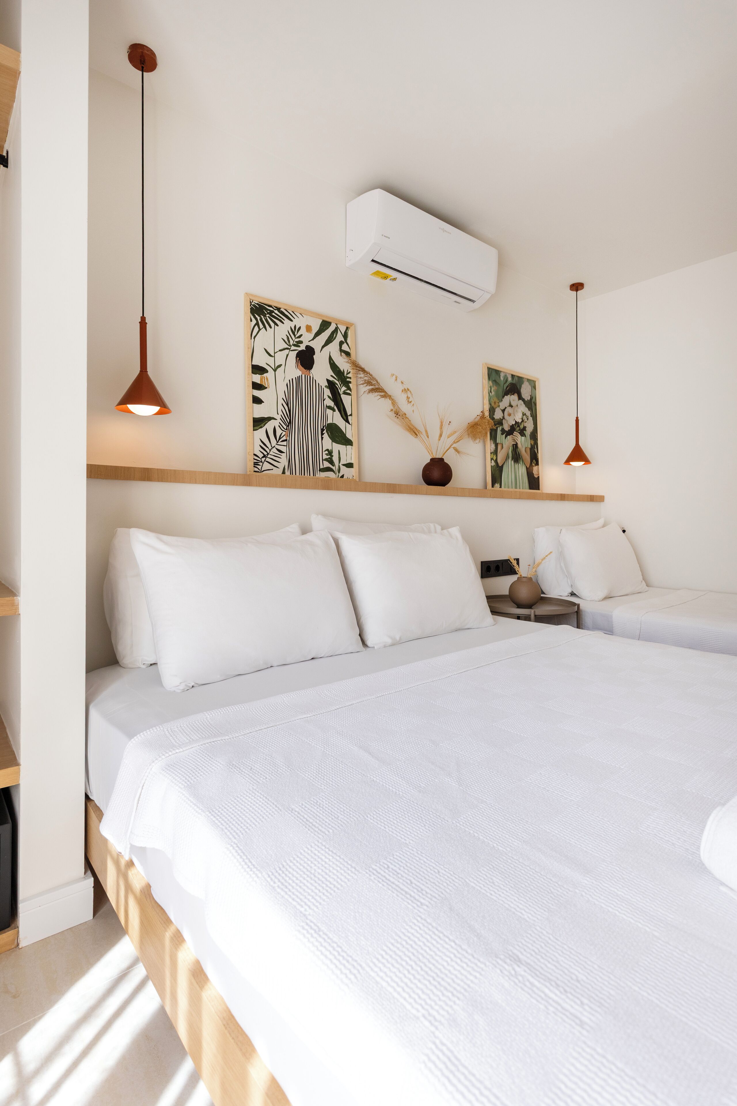 Une chambre d’hôtel avec deux lits, une tête de lit en bois, un climatiseur fixé au mur et une étagère ornée d’objets décoratifs.