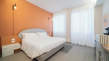 A modern bedroom with a large bed, a bedside table, a wall-mounted lamp, and a window with curtains.