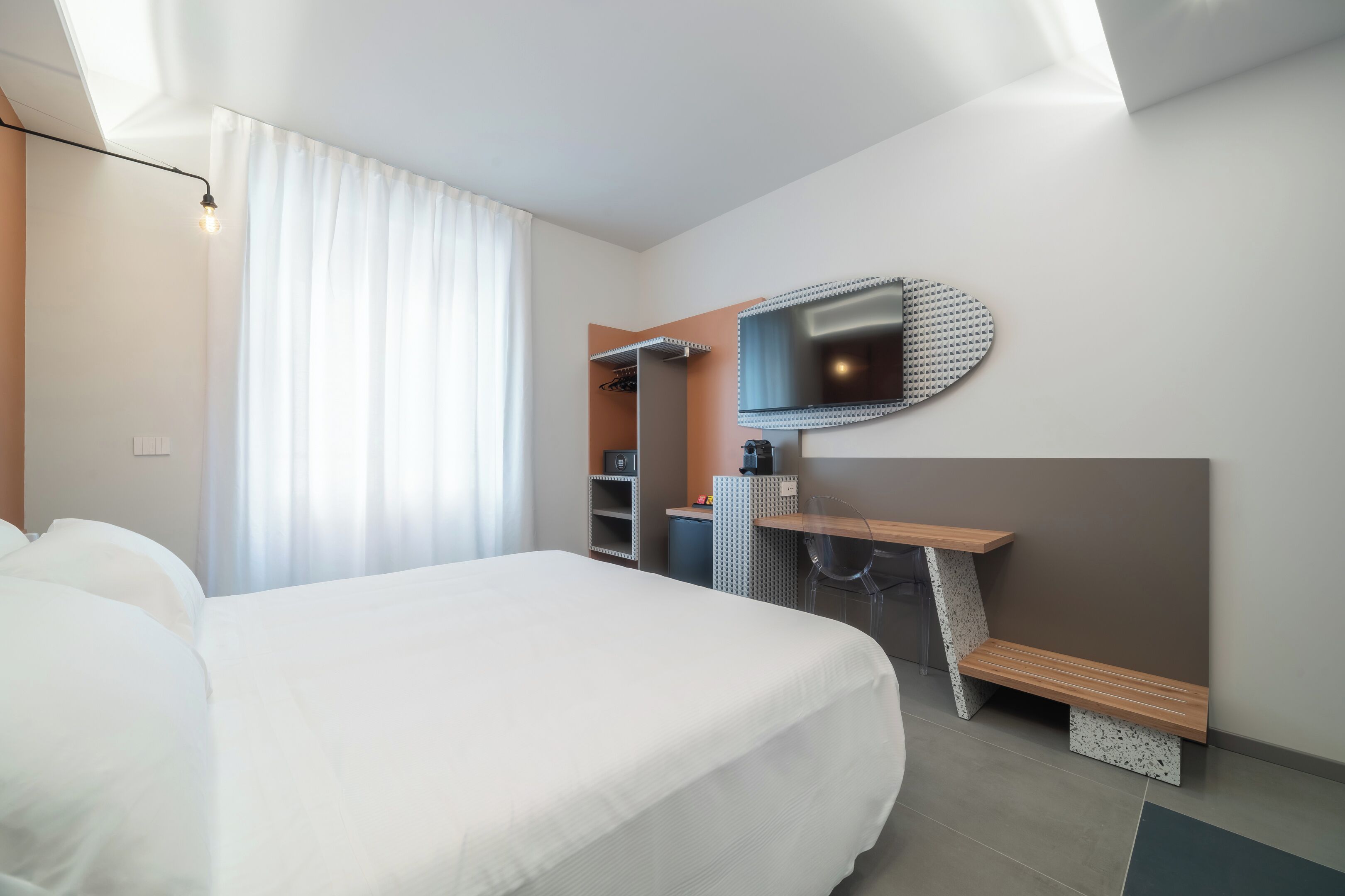 Una habitación de hotel moderna con una cama grande, un escritorio con una silla, un espejo y un armario.
