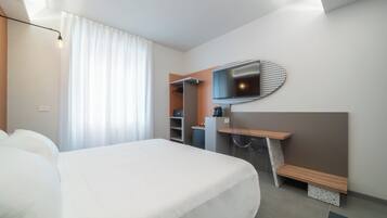 Una habitación de hotel moderna con una cama grande, un escritorio con una silla, un espejo y un armario.