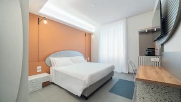 A modern hotel room with a bed, a desk, a TV, and a window with curtains.