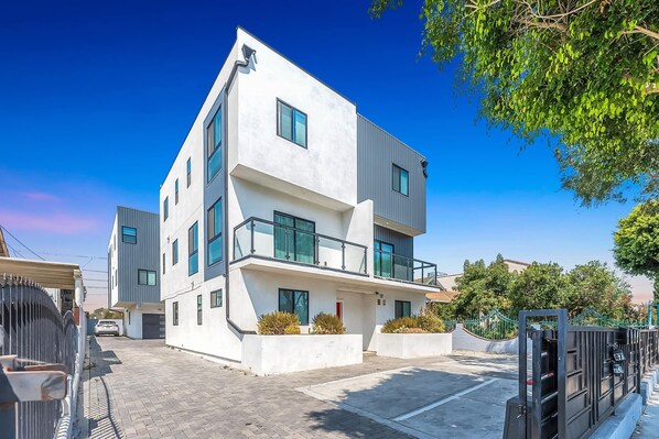 Un immeuble moderne à plusieurs étages, doté d’une façade blanche, de grandes fenêtres et d’un balcon.