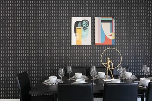 Un coin repas avec un mur noir à texture, une table dressée avec de l’assiette et des verres blancs, et une statue dorée.