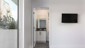 Een modern appartement met keuken, een aan de muur bevestigde televisie en een balkon met uitzicht op gebouwen en bomen.