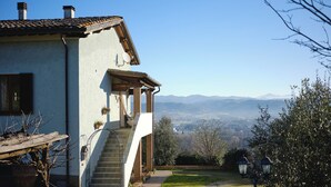 A house with a stone staircase leading to a wooden porch, a garden with a gravel path, and a view of distant mountains.
