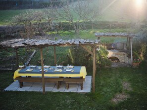 Un área de comedor al aire libre con una pérgola y un hogar a leña de piedra.