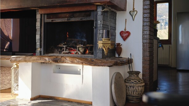A stone fireplace with a rustic mantel, a large vase, and a heart-shaped decoration on the wall.