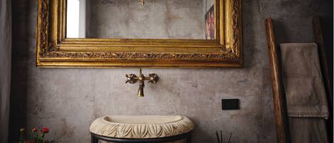A bathroom with a large ornate mirror, a pedestal sink, a chandelier, and a wooden towel rack.