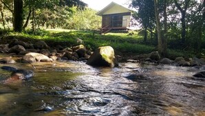Un arroyo con rocas, un puente de madera y un edificio al fondo.
