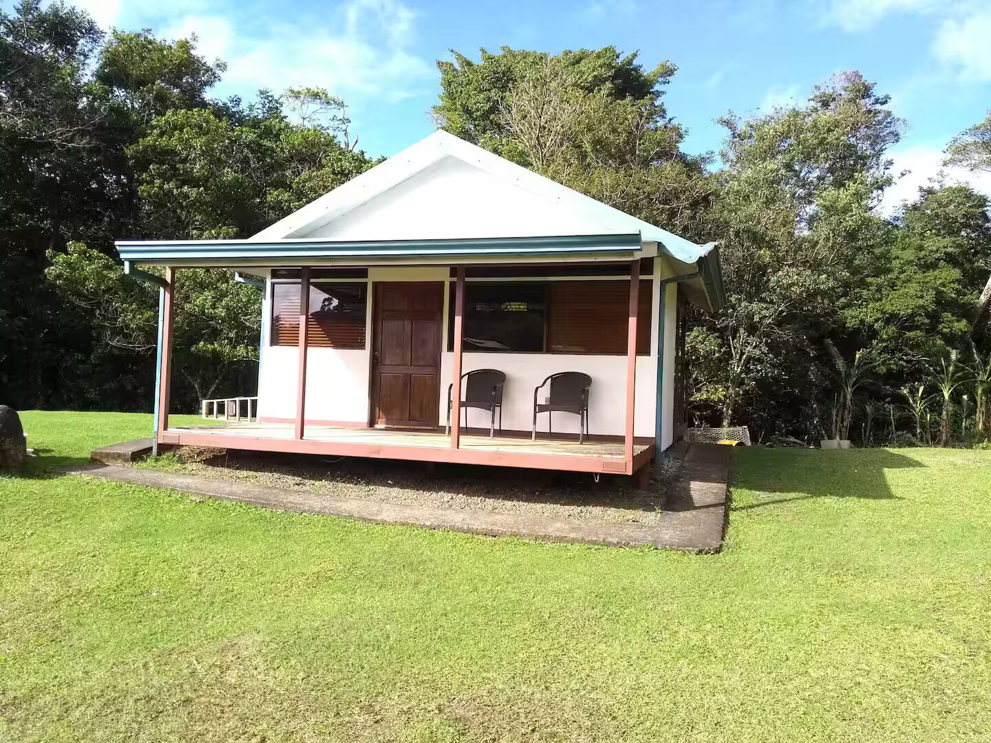 Een klein, gelijkvloers huis met een veranda en twee stoelen.