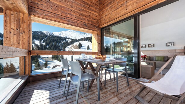 A wooden deck with a table and chairs, a hammock, and a view of snow-capped mountains. - 3-room deluxe vacation apartment (Churwalden)