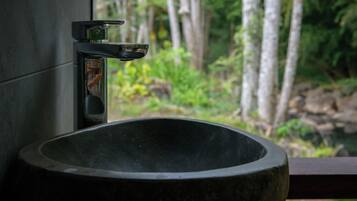 Un évier en pierre surmonté d’un robinet moderne, le tout mis en valeur par un décor de forêt luxuriante et verdoyante.
