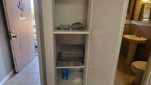 A hotel room with a wardrobe containing folded towels and a box of toiletries.
